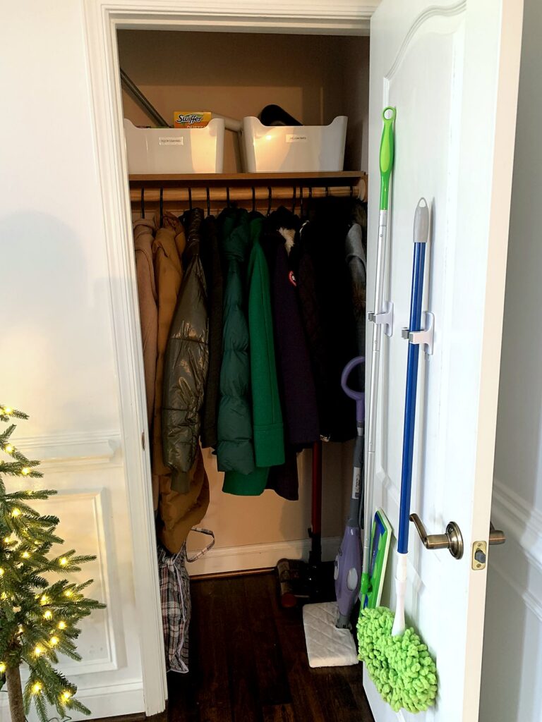 Coat closet drop zone with coats on hooks and labeled bins on the shelf above