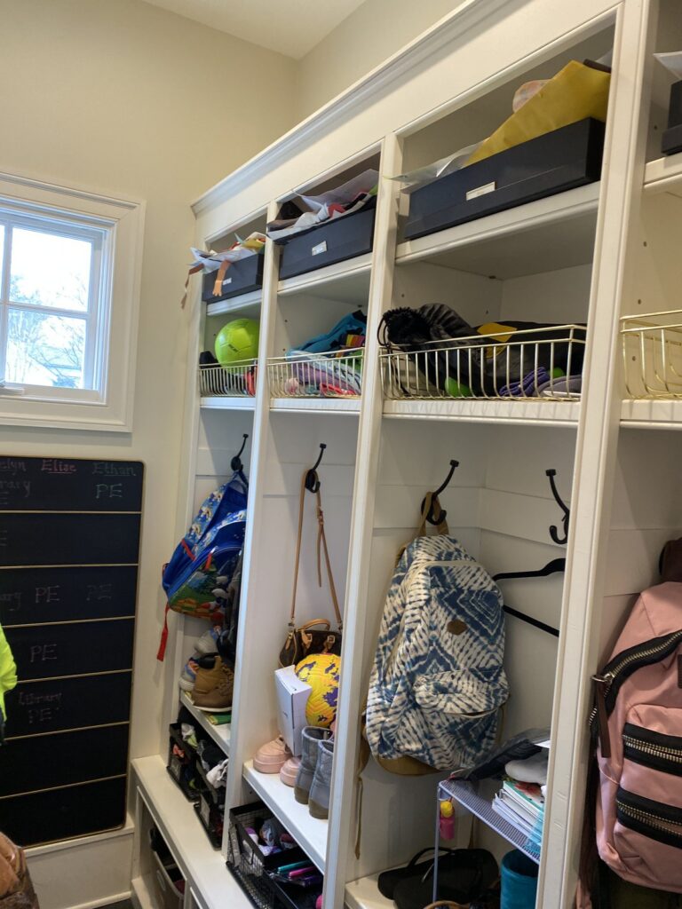Family mudroom drop zone with backpacks, sports equipment, and a labeled cubby for each kid