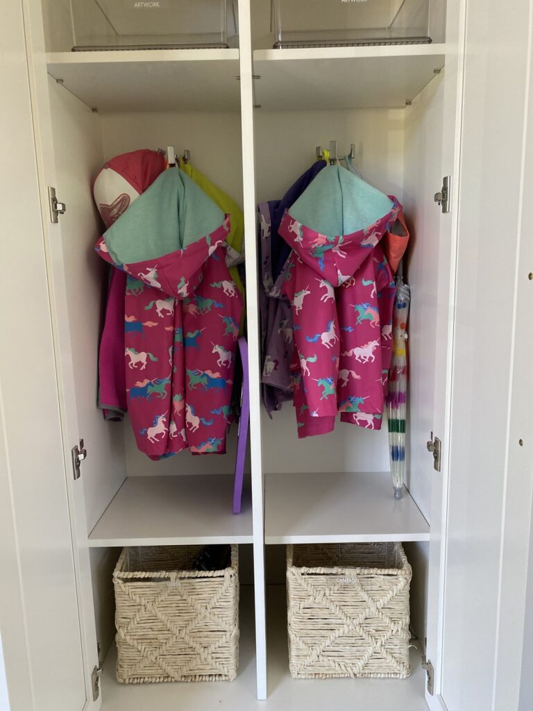 Kids' raincoats hung at kid height in mudroom lockers with woven baskets below