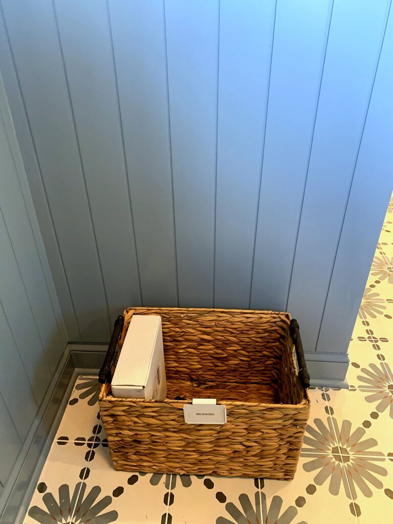 Wicker basket labeled packages by the mudroom door catching deliveries and returns
