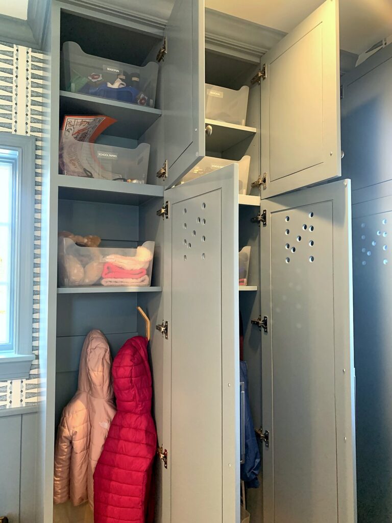 Mudroom upper cabinets and open locker with clear bins organizing kids' gear