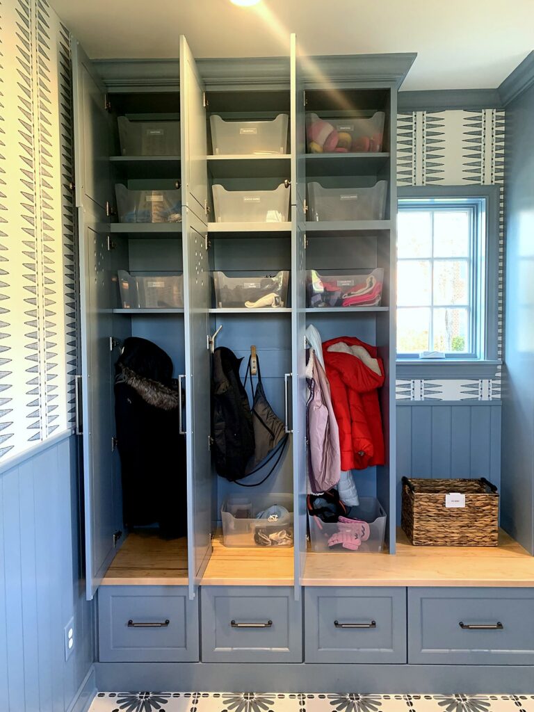 Mudroom lockers with hanging coats, clear bins, and a labeled basket on the bench