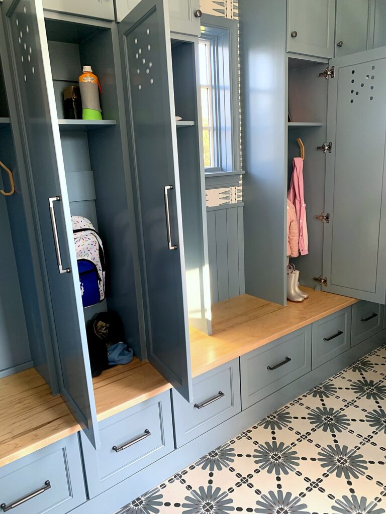 Open mudroom lockers holding a backpack, hats, and boots with shoe drawers below