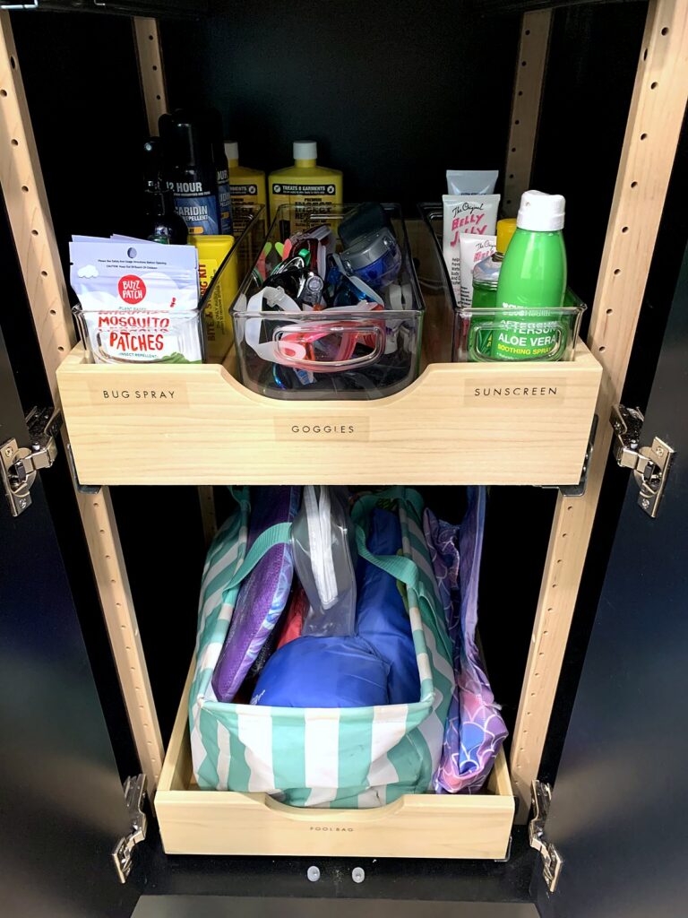 Mudroom pull-out shelves holding sunscreen, bug spray, and swim goggles for grab-and-go