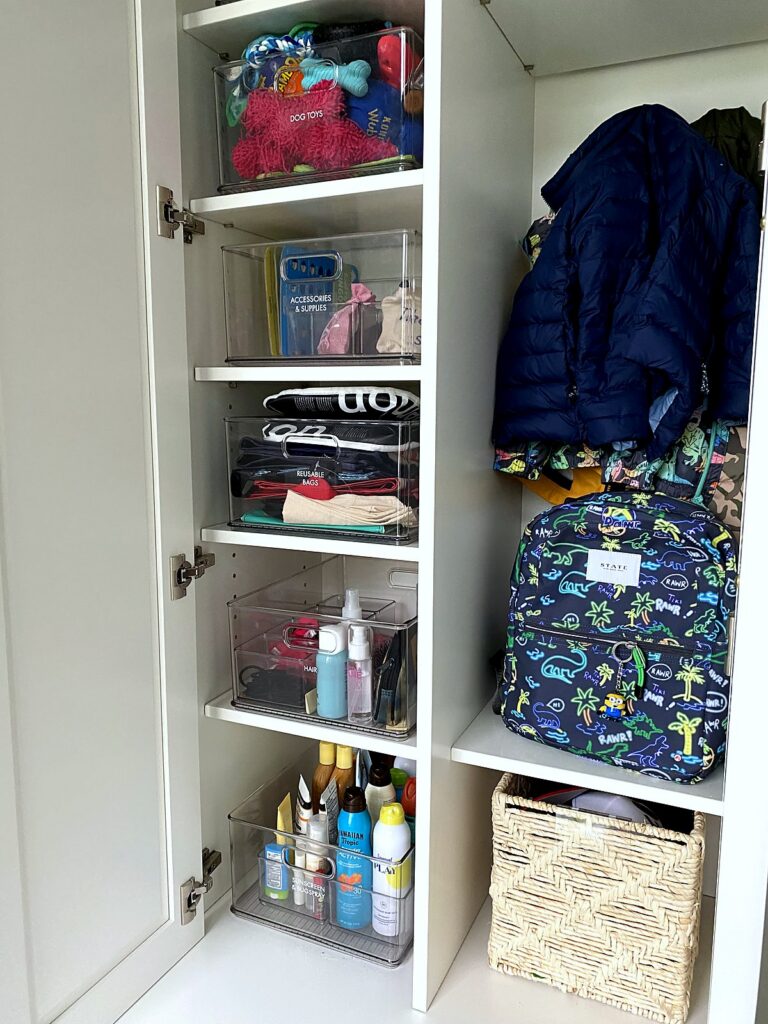 Mudroom shelves with clear bins, sunscreen bottles, and a backpack ready by the door
