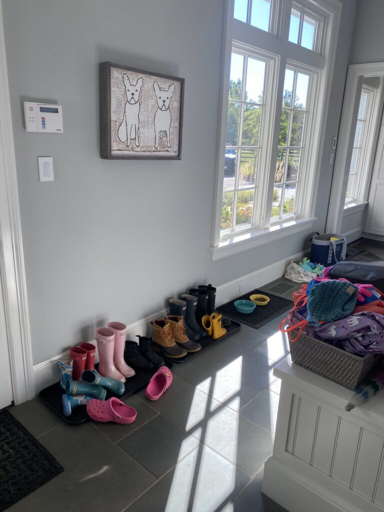 Rain boots and kids' shoes lined up on mats beside the mudroom bench