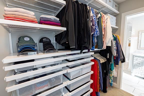 Wide view of accessible walk-in closet side featuring Elfa drawer system, sweater shelves, cap organizers, and hanging clothes