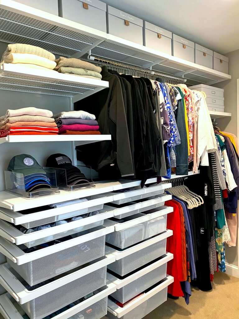 Accessible side of organized walk-in closet featuring Elfa drawer system, sweater shelves, and cap organizers after professional organization