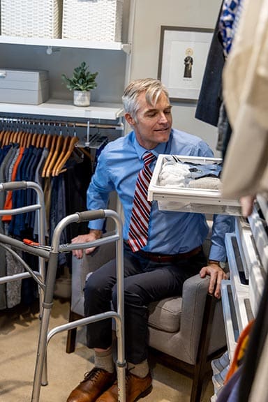 Bill seated in the closet chair accessing his Elfa drawer system with his walker nearby showing the accessible closet design
