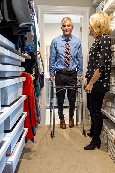 Bill walking through his newly organized accessible walk-in closet with his walker alongside his wife at the reveal