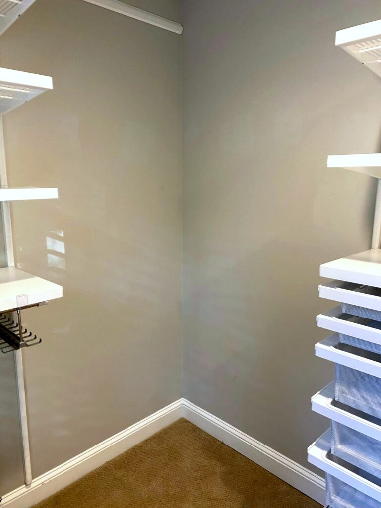 Corner view of newly installed Elfa closet system showing white shelving, clothing rod hardware, and drawer unit