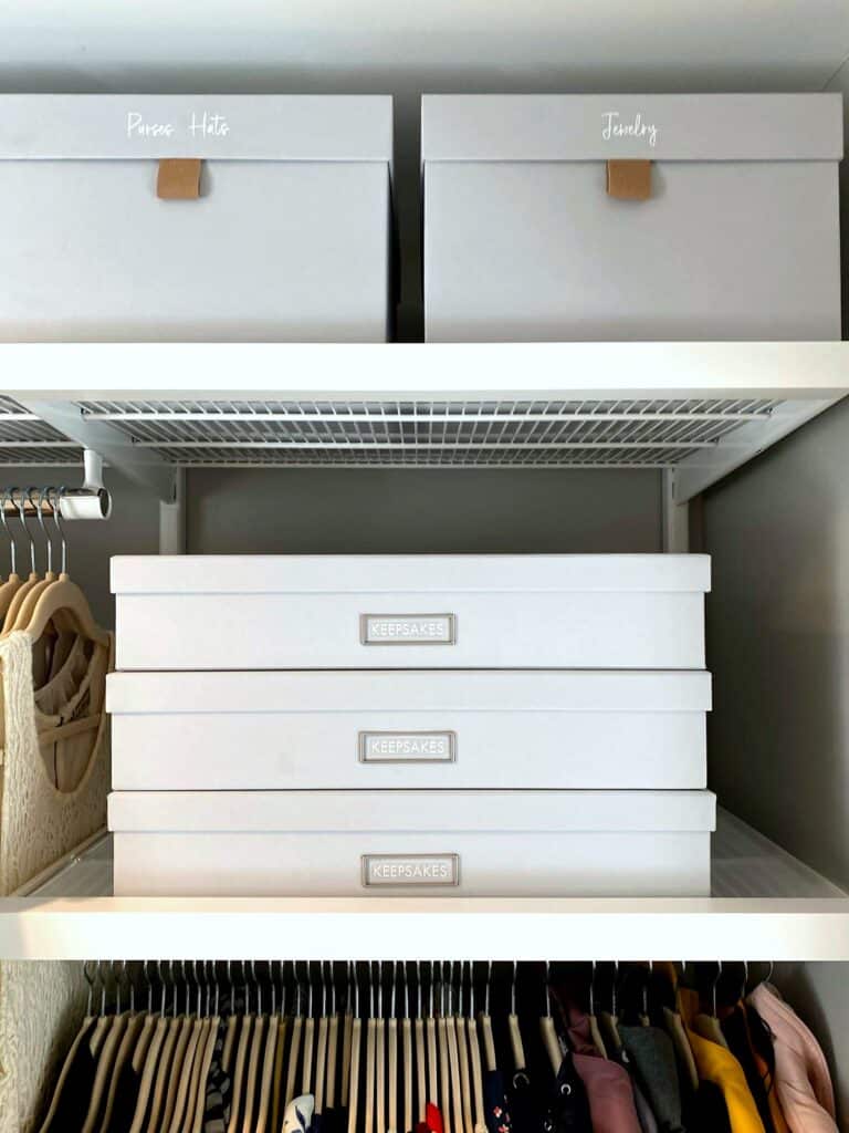 Organized closet shelf with labeled grey keepsake boxes and jewelry storage above hanging clothes after professional organization