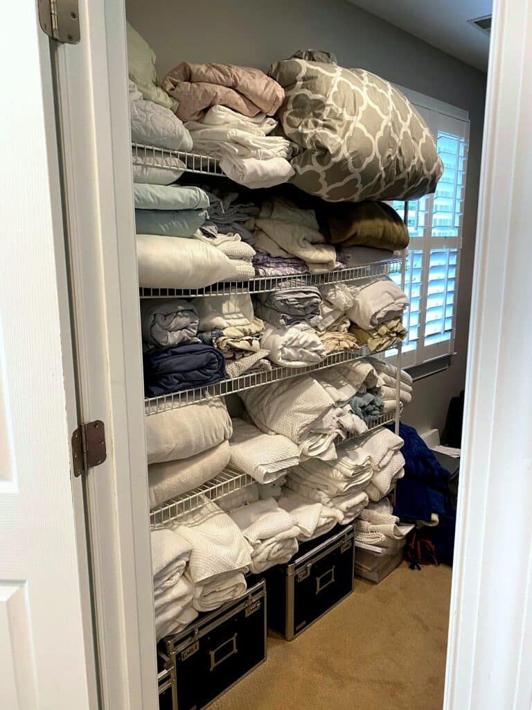 Wire shelving unit overflowing with sheets, comforters, and pillows in a walk-in closet before professional organization