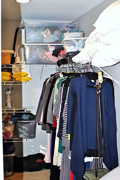 Walk-in closet with outdated wire shelving and overflowing clothes before Elfa system installation
