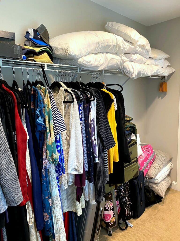 Overloaded clothing rod with hats, suitcases, and comforters piled in a walk-in closet before professional organization