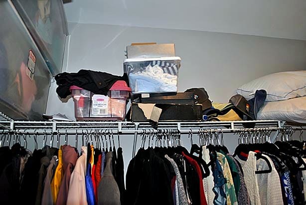 Overpacked clothing rod and cluttered shelf above in a walk-in closet before professional organization