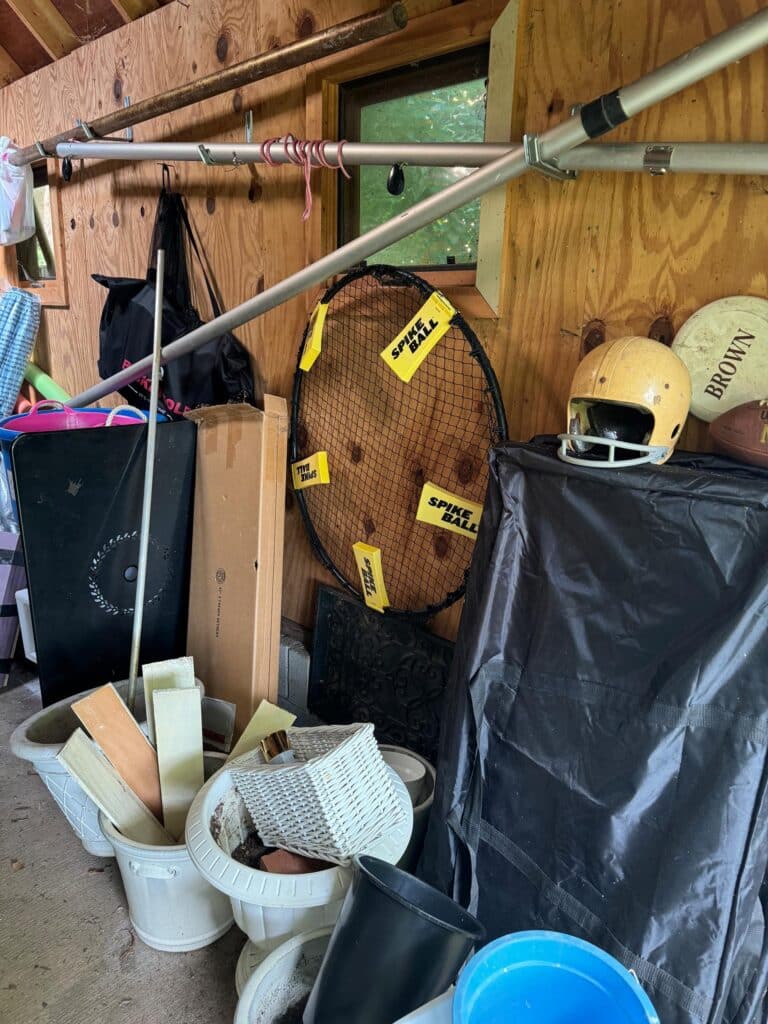 Disorganized shed interior with maypole, Spikeball, and sports equipment before professional organization