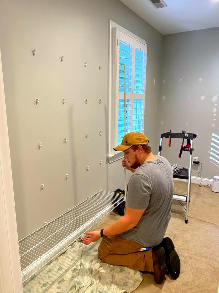 Professional installer kneeling and mounting Elfa shelving brackets on walk-in closet wall during renovation