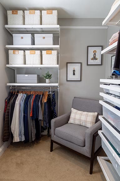 Professionally organized walk-in closet corner showing Elfa shelving, labeled baskets, grey storage boxes, and reading chair