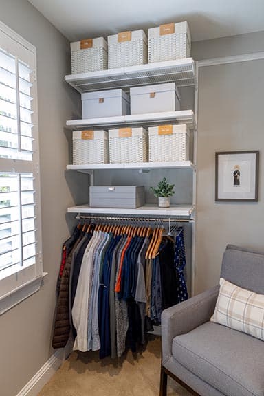 Bills section of the organized walk-in closet with warm-hanger clothing rod, labeled wicker baskets, and grey storage boxes