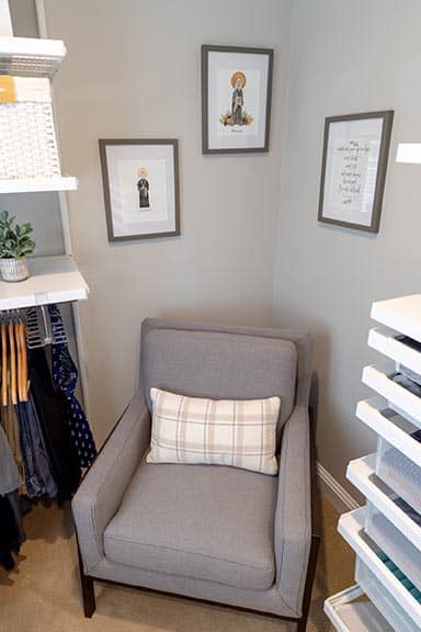 Professional photo of grey reading chair with plaid pillow and three framed religious art pieces in organized closet corner