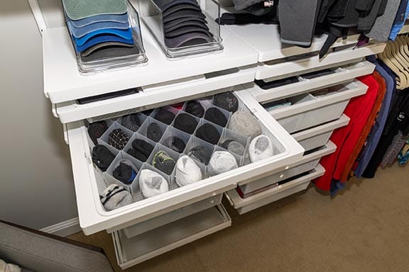 Close-up of organized sock drawer with divider inserts and clear acrylic hat organizers above in an Elfa closet system