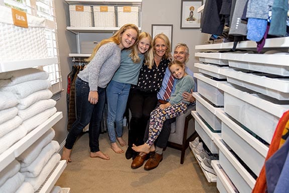 The Swick family with parents and three children smiling together in their newly organized walk-in closet