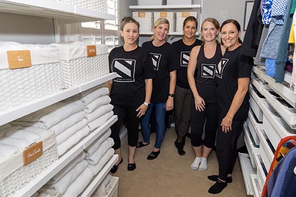 Five Systems by Susie professional organizers in matching black shirts smiling in the finished walk-in closet linen area