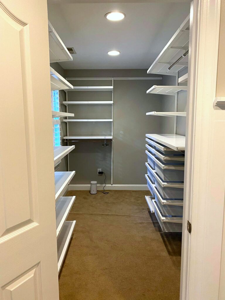 Wide view of walk-in closet with fully installed empty Elfa shelving system including drawers, shelves, and hanging rods