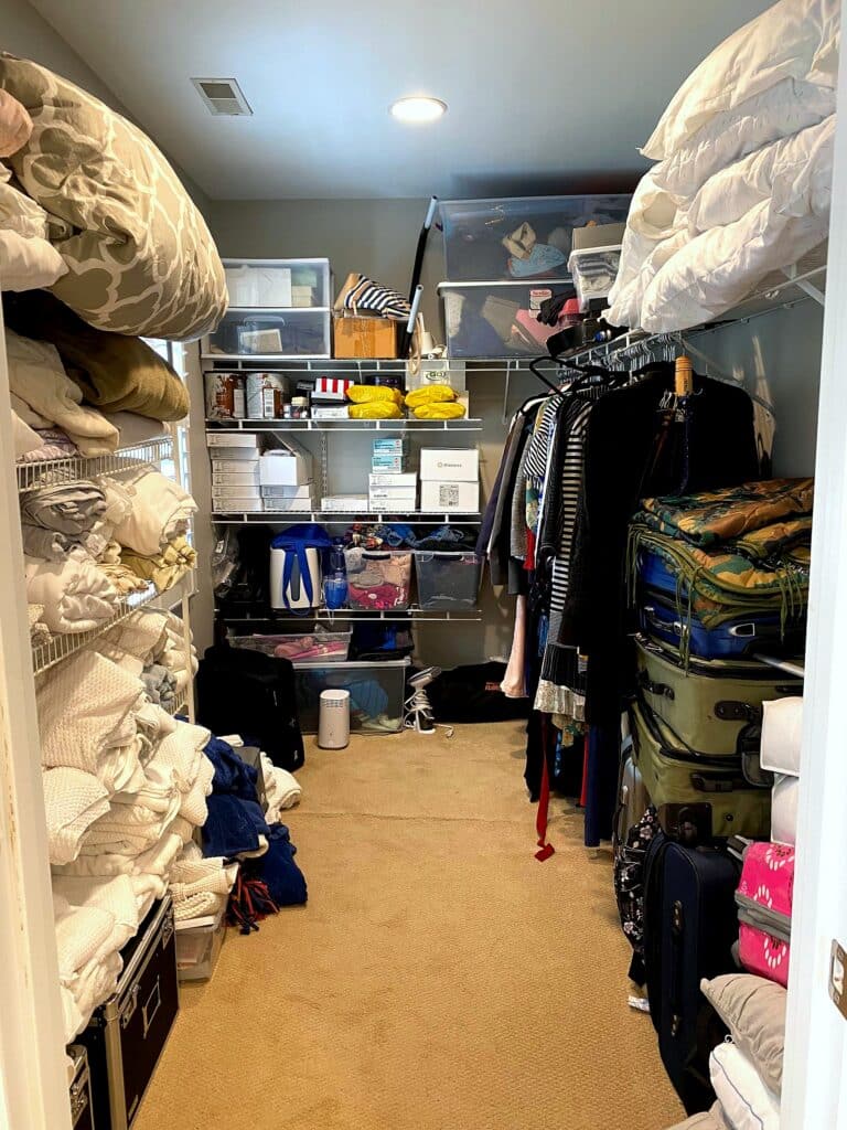 Full length view of disorganized walk-in closet showing linen side, medical supply shelving, and clothing area before professional organization