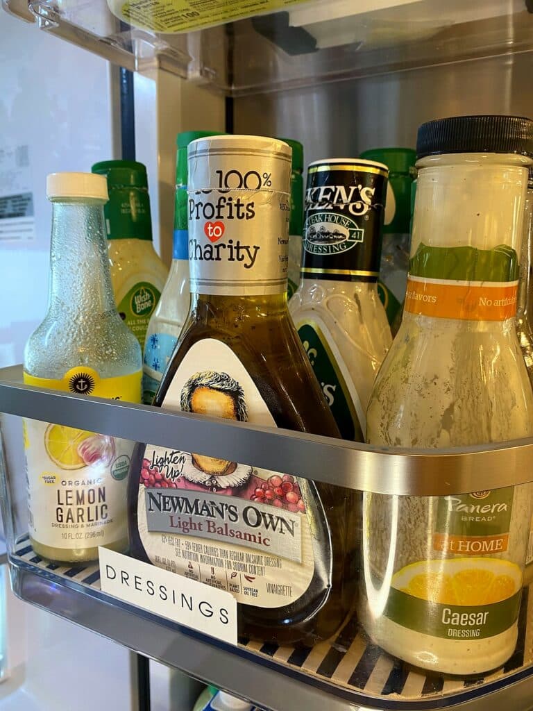 Refrigerator door bin labeled Dressings with lemon garlic, Newman's Own, Ken's, and Panera caesar bottles