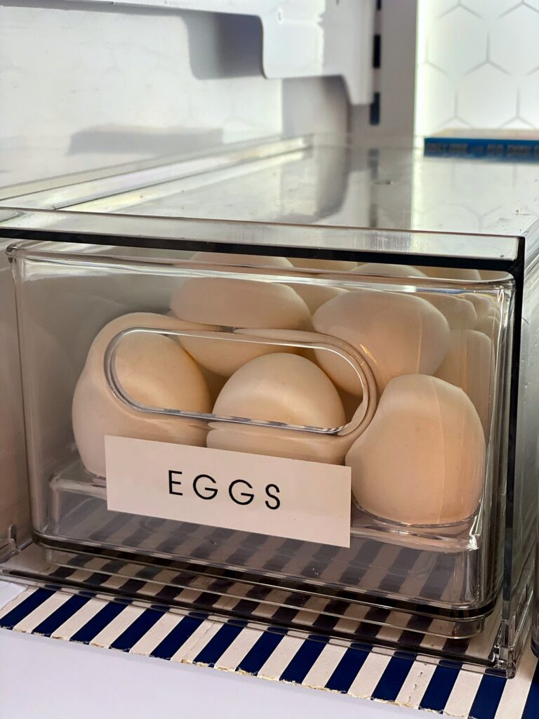 Clear pull-out bin of eggs labeled Eggs sitting on a navy striped fridge coaster liner