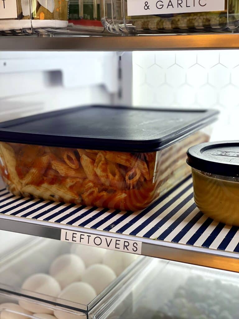 Glass leftovers container of pasta on a striped fridge coaster below a Leftovers label