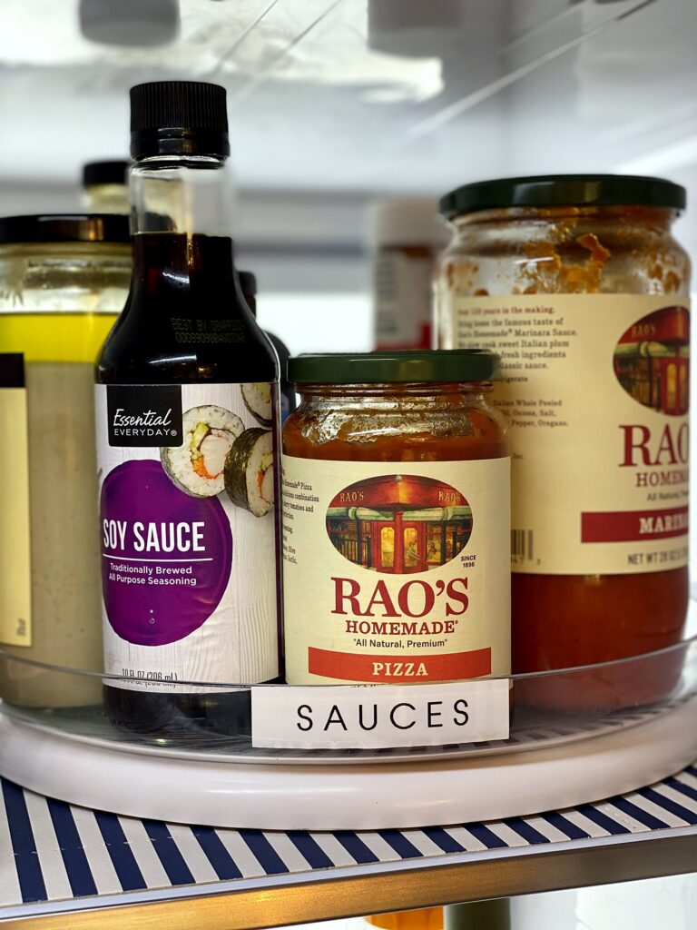 Refrigerator lazy Susan turntable labeled Sauces holding soy sauce and Rao's pizza and marinara sauces