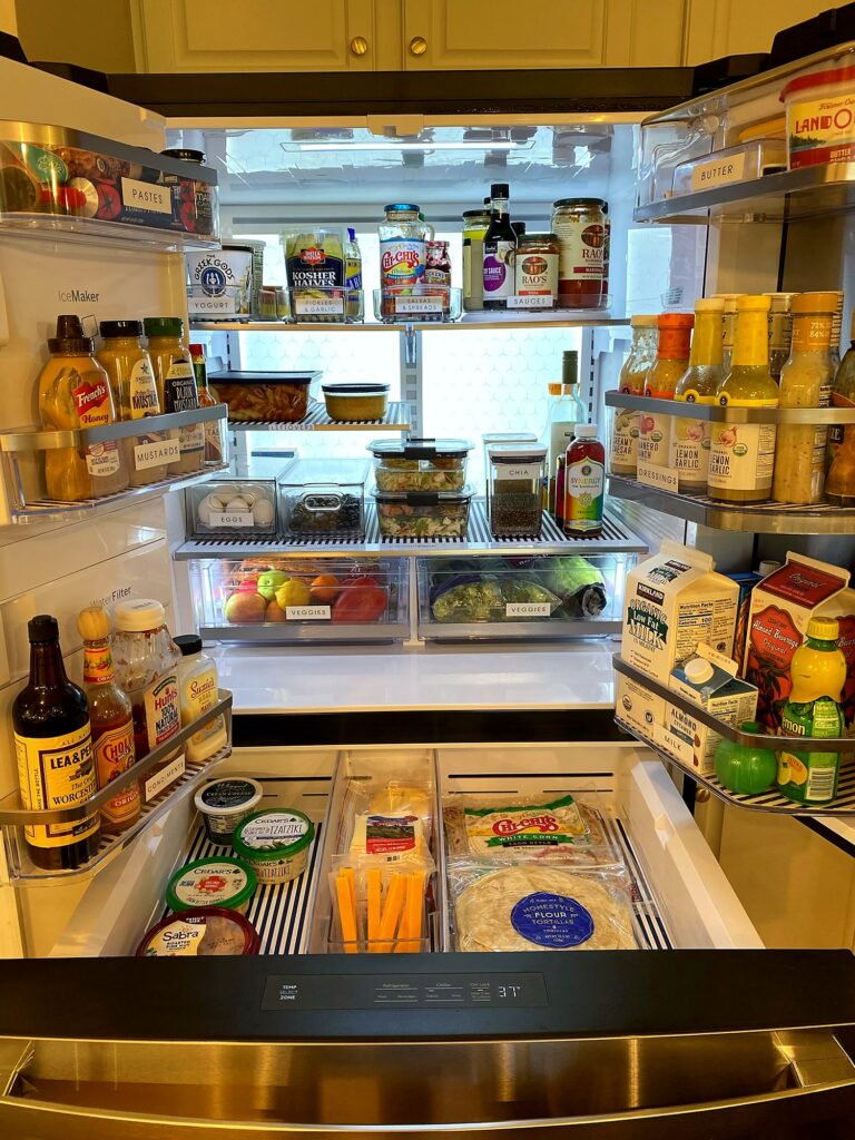 Fully organized GE Profile refrigerator with labeled zones, clear bins, and striped fridge coasters, doors open