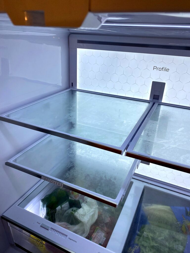 Empty adjustable glass refrigerator shelves in a GE Profile fridge during an organizing setup