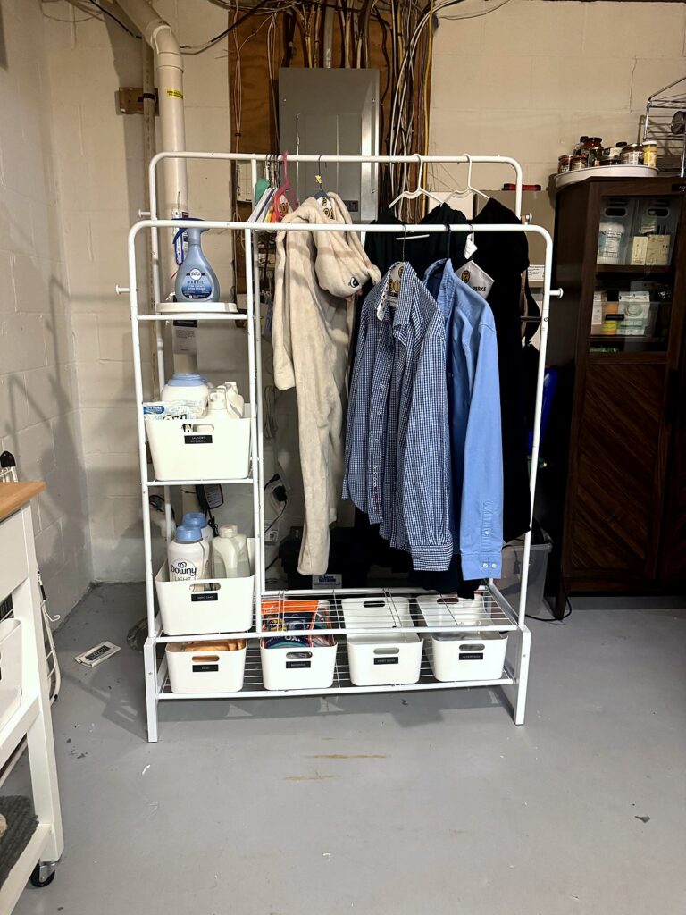 Rolling clothes rack for air drying shirts with labeled white bins in a basement laundry room