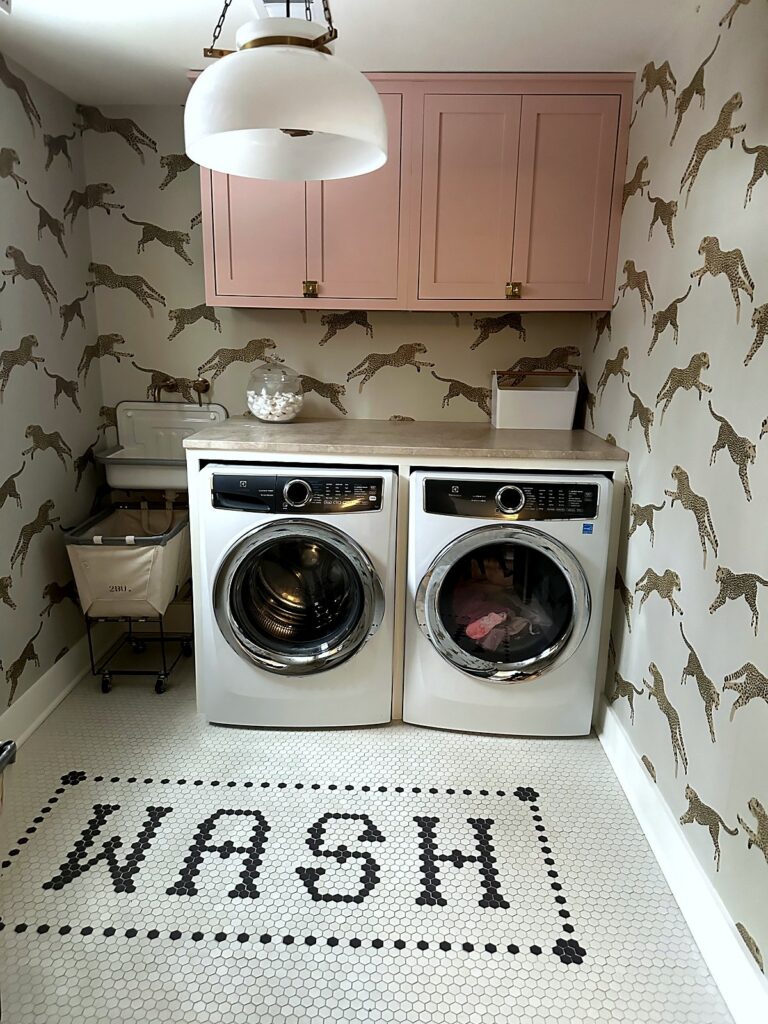 Cheetah print wallpaper laundry room with pink cabinets and WASH spelled out in penny tile
