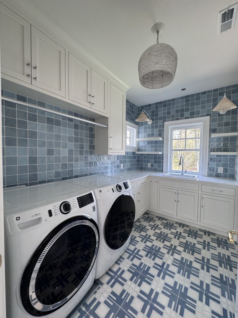 White laundry room with blue tile backsplash, open shelves, and washer and dryer on a patterned floor