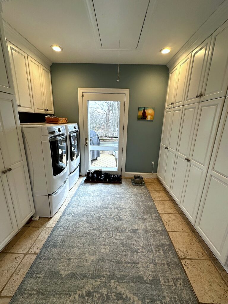 Long laundry room with floor-to-ceiling white storage cabinets and a soft rug after organization
