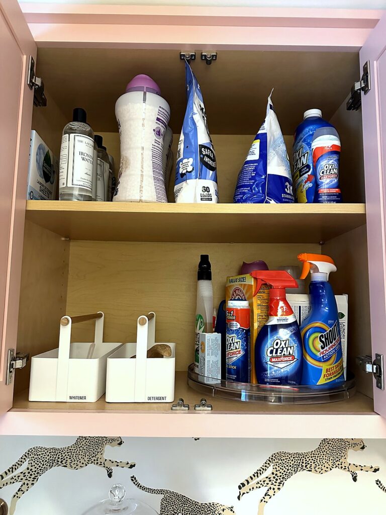 Lazy Susan and white caddies corralling stain removers and laundry supplies inside a pink cabinet
