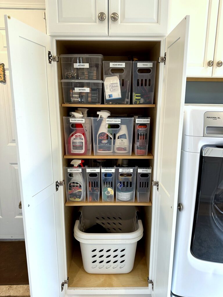 Tall laundry room cabinet with labeled clear bins for supplies and a laundry basket below